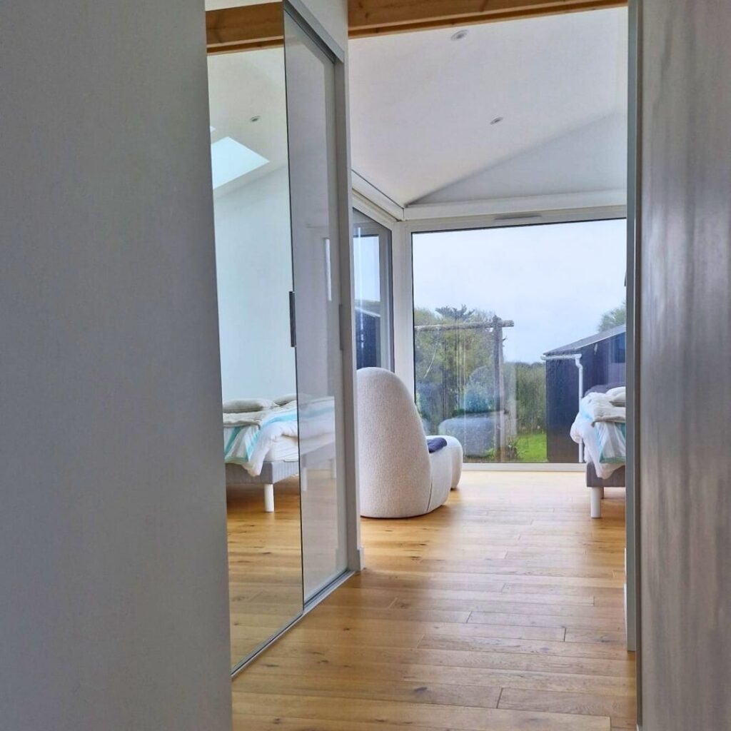 Extension contemporaine à bardage bois et aluminium noir, avec grandes fenêtres panoramiques, accolée à une maison traditionnelle et donnant sur un jardin.