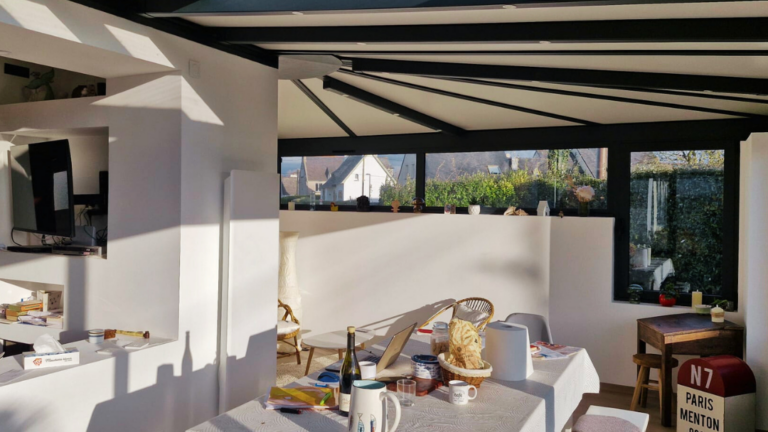 Véranda moderne avec structure en aluminium noir et toiture vitrée, aménagée en salle à manger lumineuse ouverte sur le jardin.